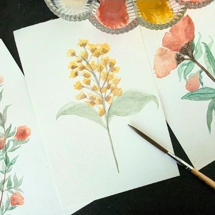 Watercolor flower paintings in progress, with a brush and a palette of red and yellow paints.